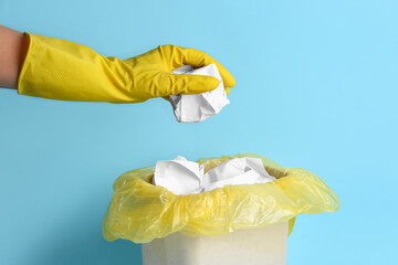 Woman throwing crumpled paper into rubbish bin on color background