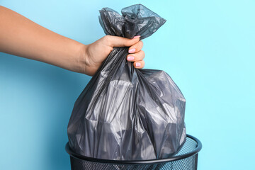 Woman taking garbage bag out of rubbish bin on color background, closeup