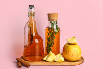 Wooden board with bottles of fresh apple juice with rosemary and fruits on color background