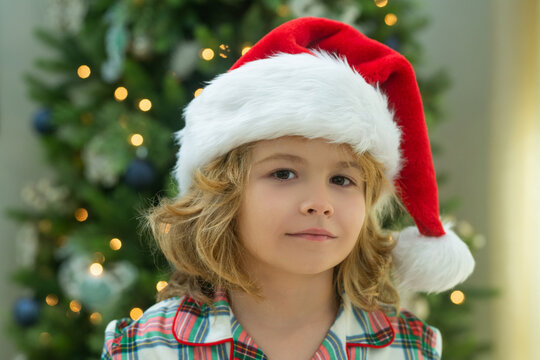 Close up portrait. Happy funny child in Santa hat near Christmas tree. Christmas and New Year concept.