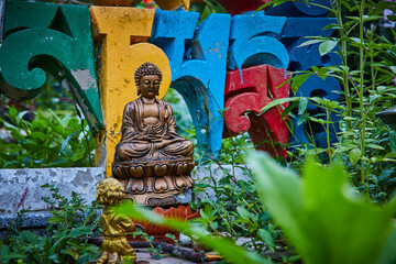 Greenery surrounds small Buddha statue and colorful lettering
