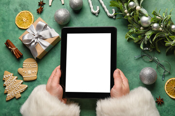 Santa Claus with tablet computer, Christmas decor and treats on green background