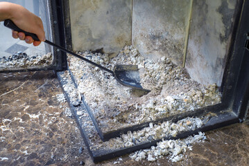 Cleaning the fireplace. Ash and charred piece of wood lying on the blade with a long handle closeup