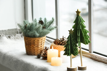 Toy Christmas trees, candles, fir cones and branches on windowsill in room, closeup