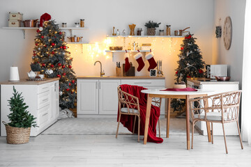 Interior of kitchen with glowing Christmas trees, counters and dining table
