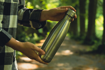 Close-up of Unrecognizable female hand holding Water bottle. Reusable steel thermo water bottle in...