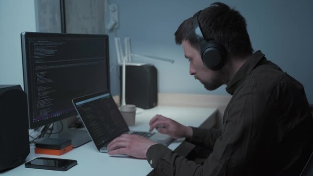 Concept of smartworking in lockdown. Man programmer in headphones sitting at at computer workplace at home office . Coding, programming. Software engineer working on programming code for new project.