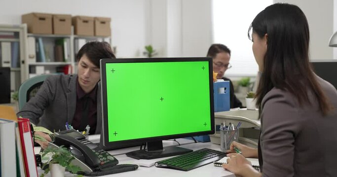 view from behind concentrated female employee taking and writing information on a memo note from computer with chroma kay mockup in the office with coworkers