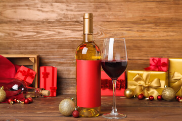 Bottle of wine with glass and Christmas balls on wooden background, closeup