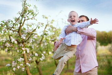 Fototapeta premium Happy father with a little son in a blooming garden. Dad's Day. Throw the child up.