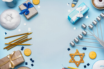 Frame made of menorah, gifts, Jewish hat and treats for Hannukah celebration on blue background