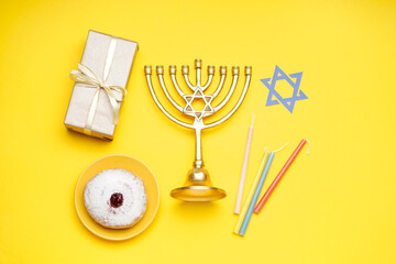 Menorah with doughnut, candles, David star and gift for Hannukah celebration on yellow background