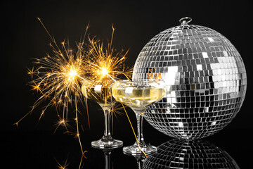 Glasses of champagne with Christmas sparklers and disco ball on black background