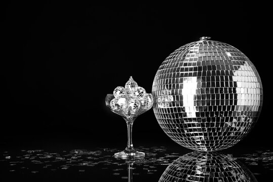 Glass with disco balls and confetti on black background