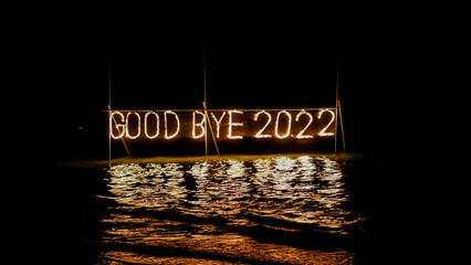good bye 2022 burning phrase made of fire stick placed on water in sea, happy new year celebration in tropical place at night, inscription on the beach, reflection 
