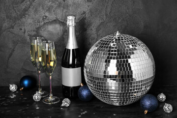 Disco ball with Christmas toys, bottle and glasses of champagne on dark background