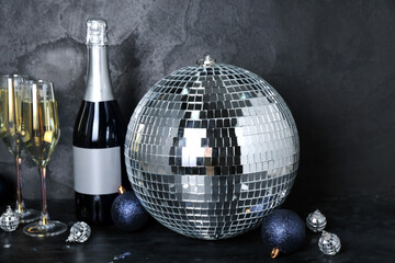 Disco ball with Christmas toys, bottle and glasses of champagne on dark background