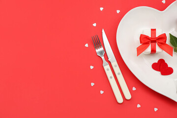 Table setting for Valentine's Day with gift and hearts on red background