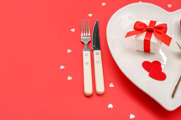 Table setting for Valentine's Day with gift and hearts on red background