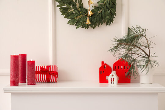 Vase with Christmas branches, house shaped candle holders and gift on mantelpiece in room