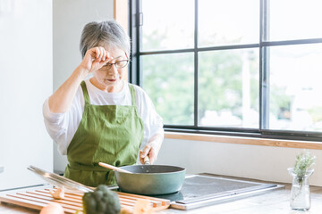 家のキッチンで料理を作るアジア人の高齢者女性（認知症・悩む）  © buritora