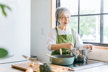 家のキッチンで料理を作るアジア人の高齢者女性（笑顔）
