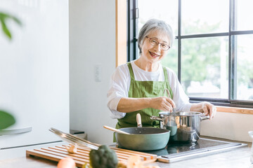 家のキッチンで料理を作るアジア人の高齢者女性（笑顔・カメラ目線）
