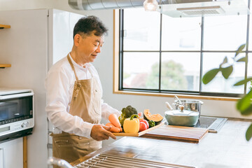 家のキッチンで野菜を使って料理するアジア人中高年・高齢者男性
