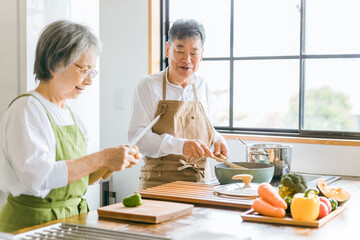 家のキッチンで一緒に料理・家事を楽しむ高齢者夫婦・シニアカップル
