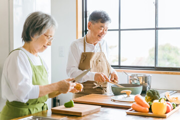 家のキッチンで一緒に料理・家事を楽しむ高齢者夫婦・シニアカップル
