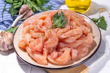 Cooking diet white poultry meat background. Fresh sliced chicken strips raw for cooking, with spices, herbs, on a white tile background top view copy space