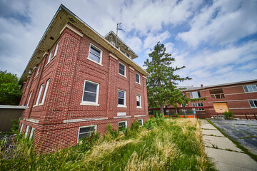 Three story abandoned brick buildings with overgrown fields