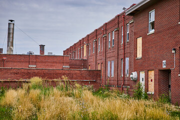 Fototapeta na wymiar Exterior of abandoned brick buildings with overgrown fields