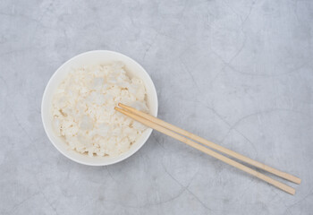 Cooked white rice in white bowl with wood sticks on grey background. Selective focus. Asian food concept