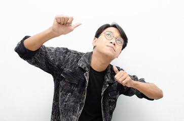 handsome attractive Asian man wearing jeans jacket smiling happily and giving thumbs up as...