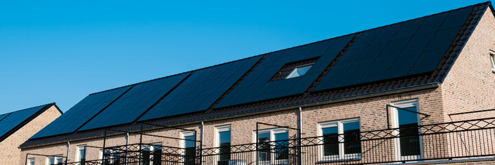 House with black solar panels attached to the roof against a sunny blue sky in the Netherlands. Sun...