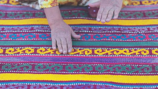 Hands of an old woman stroking a handmade carpet by ancient technologies with an Asian pattern