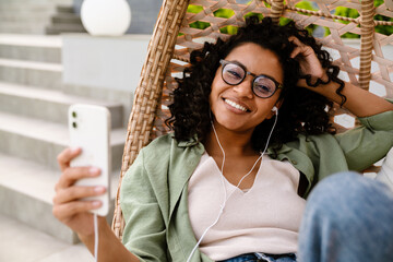 Cheerful african american woman using smartphone while sitting outdoors