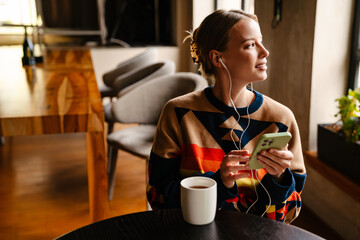 Young woman listening music with earphones and smartphone and drinking tea in cafe