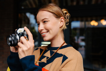 Cheerful woman taking photo on retro camera while walking outdoors