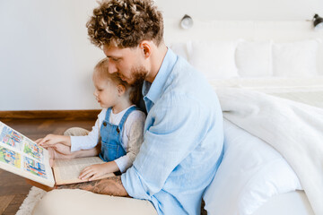 Naklejka premium Young white father and little daughter reading book together at home