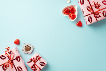 Valentine's Day concept. Top view photo of present boxes in wrapping paper with kiss lips pattern and heart shaped tableware with chocolate candies on isolated pastel blue background with blank space