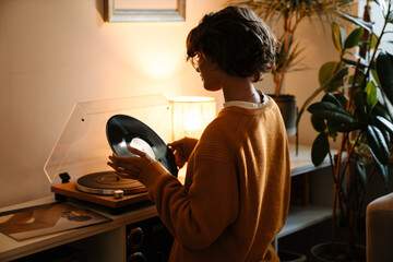 Brunette young woman in eyeglasses using stereo turntable - 553397156
