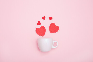 Coffee cup and red wooden hearts on a pink background. The concept of Valentine's day, love, dating and wedding. Symbol of a romantic gift or marriage proposal. Copy space, minimalism.