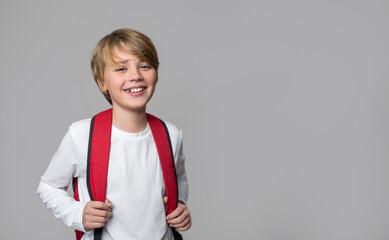Portrait of smiling preteen child with backpack, middle school age teenager in white t-shirt looking at camera over gray background. Positive mood, copy space for educational advertisement.