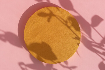 Geometric golden podium on an abstract pink background with a shadow of plant leaves. Scene for the product presentation. Showcase, display case