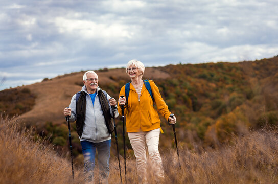 Active Senior Couple With Backpacks Hiking Together In Nature On Autumn Day.