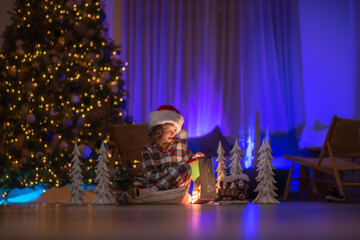 Children opening presents on Xmas eve. Lighting in magic Christmas night at cozy home. Cute child on Christmas night at home. Merry Christmas.