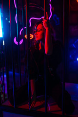 Caucasian woman in a cage in a neon studio. 