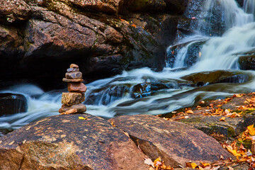 Stack of rocks cairn on edge of cascading river with fall leaves